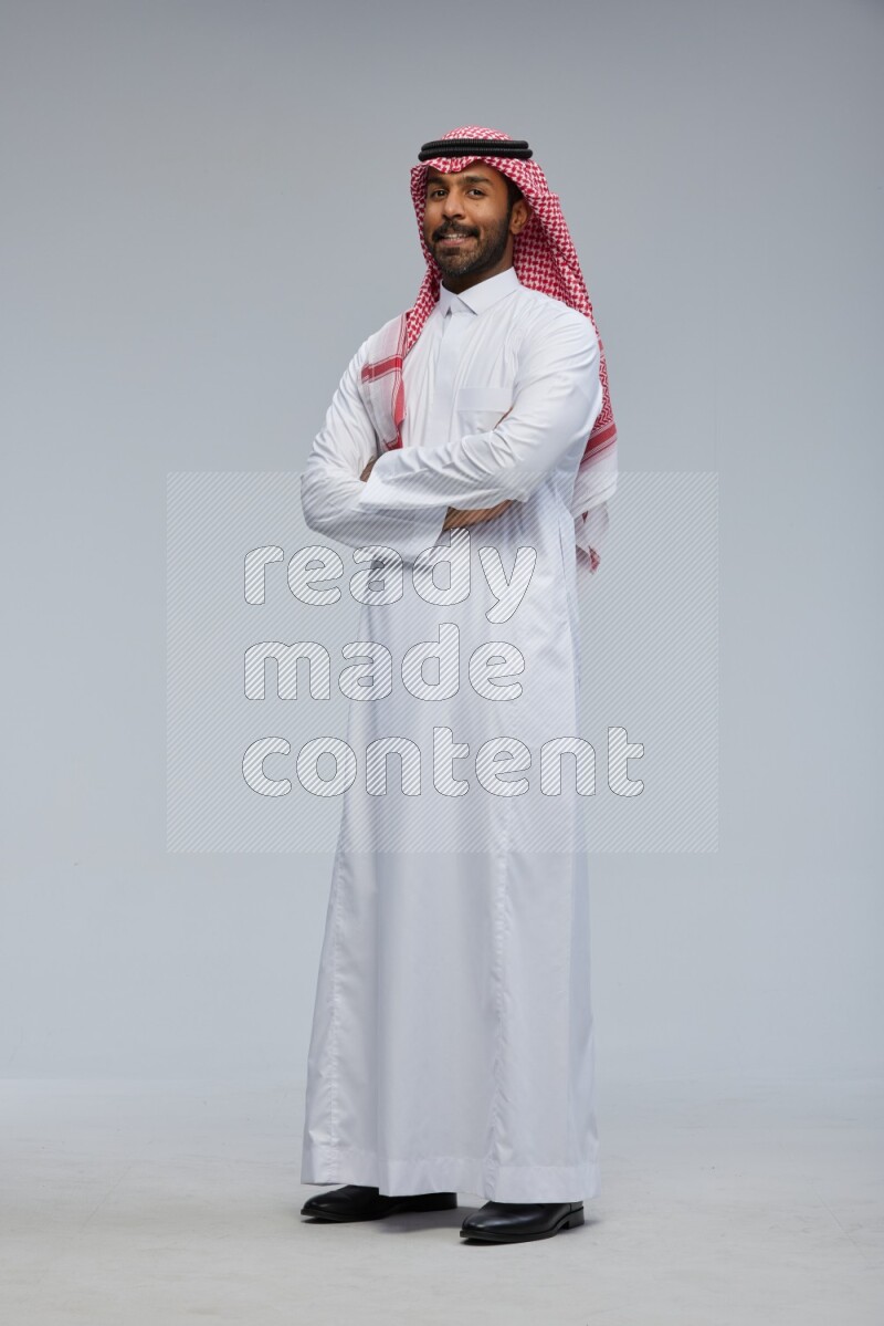 Saudi man Wearing Thob and shomag standing with crossed arms on Gray background