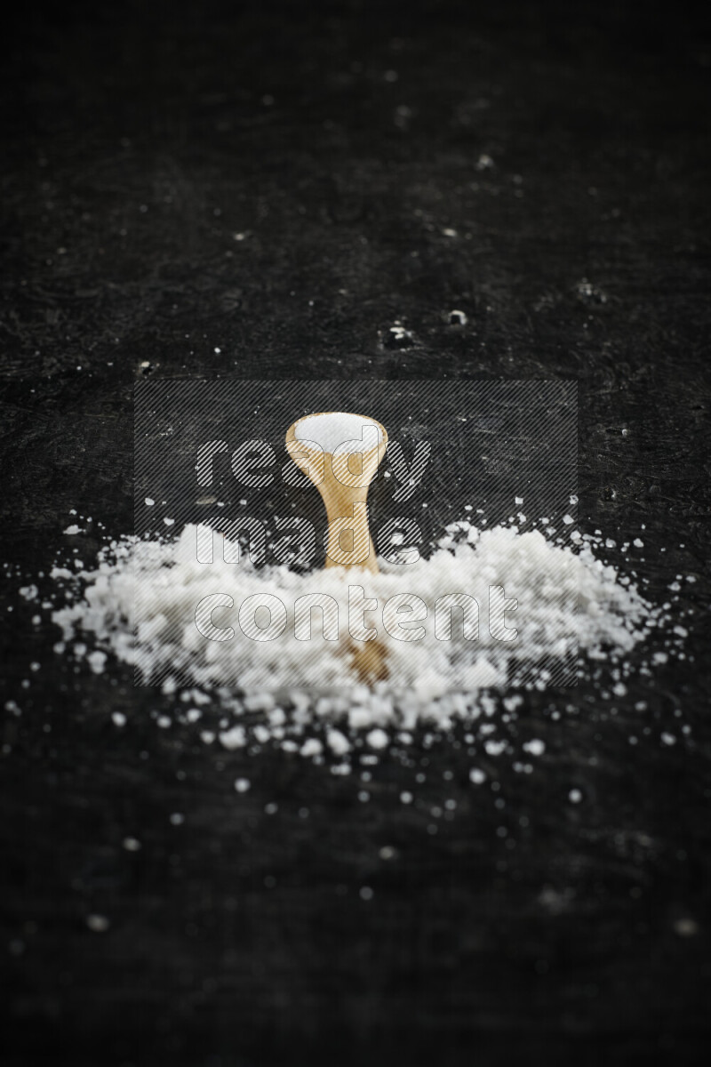 A wooden spoon full of white salt on black background
