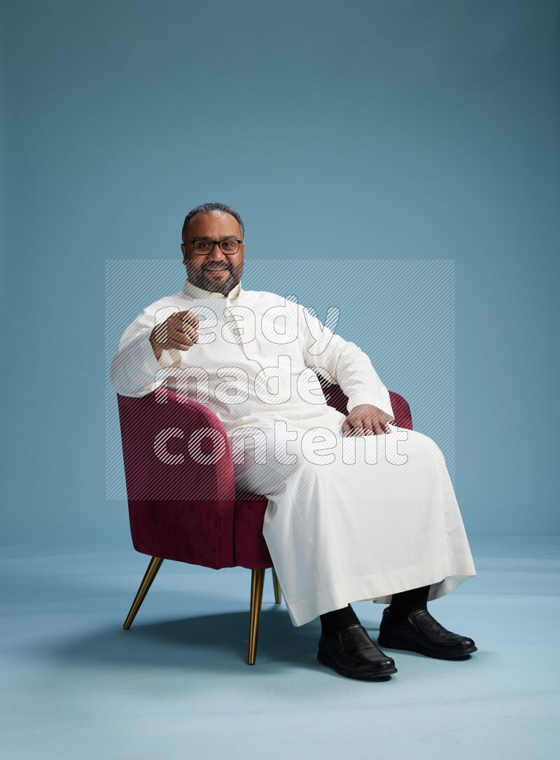 Saudi Man without shimag sitting on chair holding ATM card on blue background