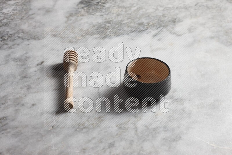 Multicolored pottery bowl with wooden honey dipper on the side on grey marble background