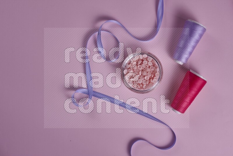 A purple and pink collection of sewing and tailoring tools arranged on a pink background