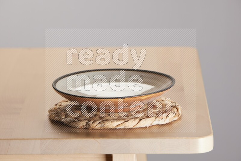 multi-colored pottery Plate placed on a small light colored straw placemat on the edge of wooden table