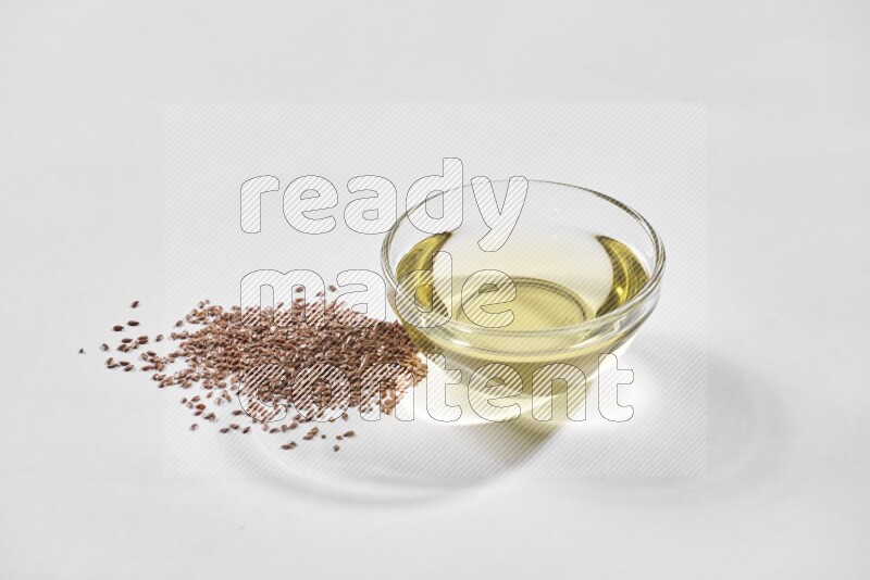 A glass bowl full of flaxseeds oil and flaxseeds beside it on a white flooring