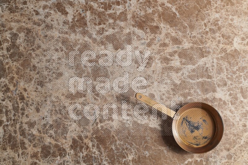 A small copper pan on beige marble background