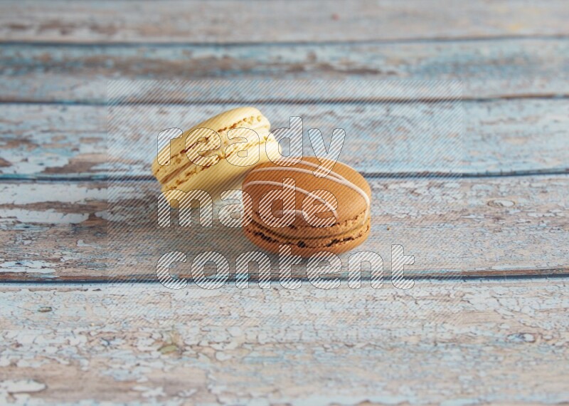 45º Shot of of two assorted Brown Irish Cream, and Yellow Vanilla macarons on light blue background