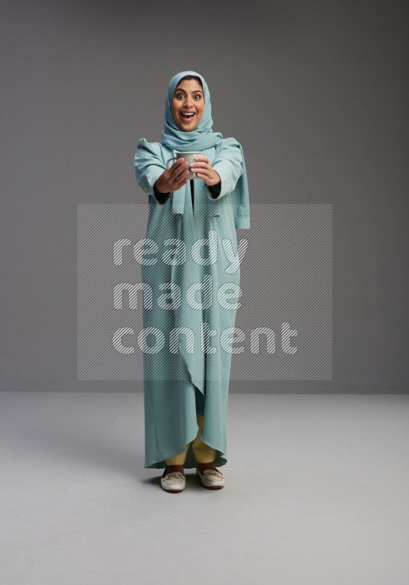 Saudi Woman wearing Abaya standing  holding a mug on Gray background