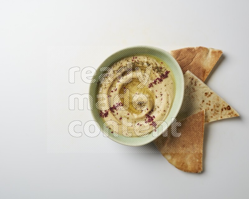 Hummus in a green plate garnished with zattar & sumak on a white background