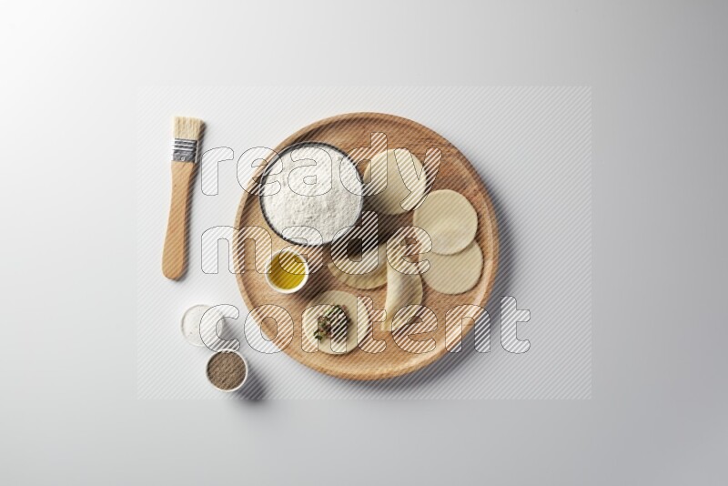 two closed sambosas and one open sambosa filled with meat while flour, salt, black pepper and oil with oil brush aside in a wooden dish on a white background