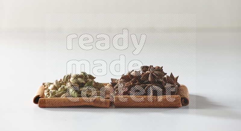 مربعان من أعواد القرفة ممتلئان باليانسون النجمي وحبوب الهيل علي خلفية بيضاء