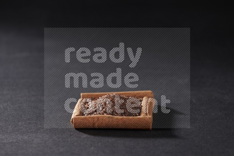 أربعة من أعواد القرفة مكونة شكل مربع بداخلها بذور الكتان علي خلفية سوداء