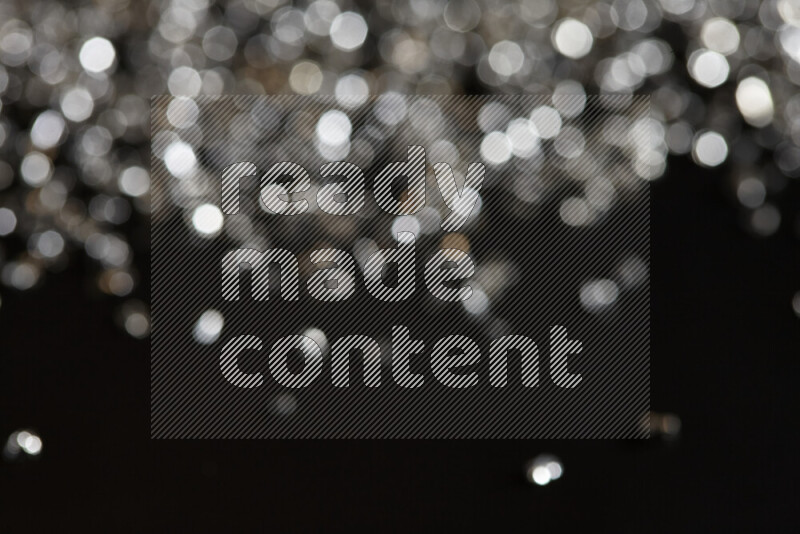 Silver shimmering fragments of glass scattered on a black background