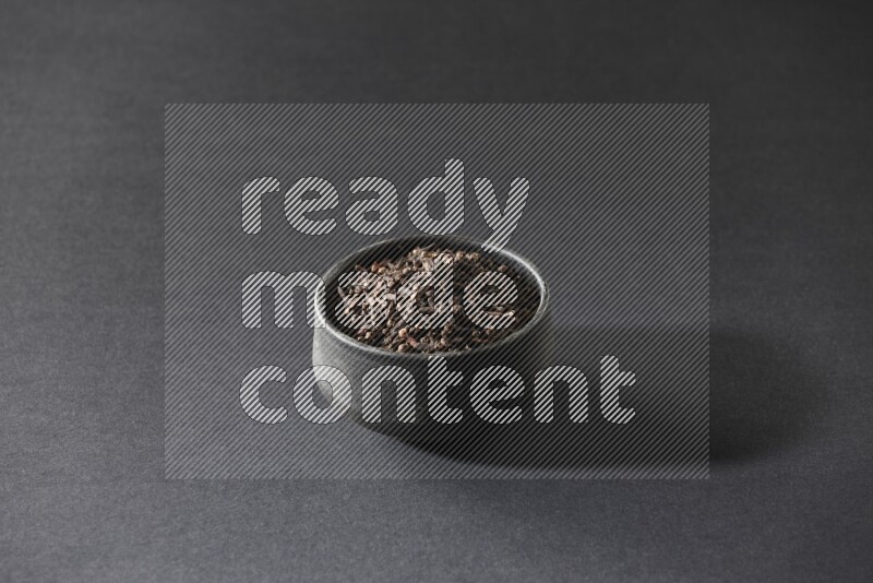 A black pottery bowl full of cloves on a black flooring