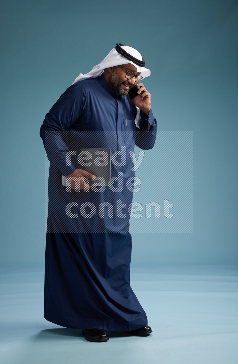 Saudi Man with shimag Standing talking on phone on blue background