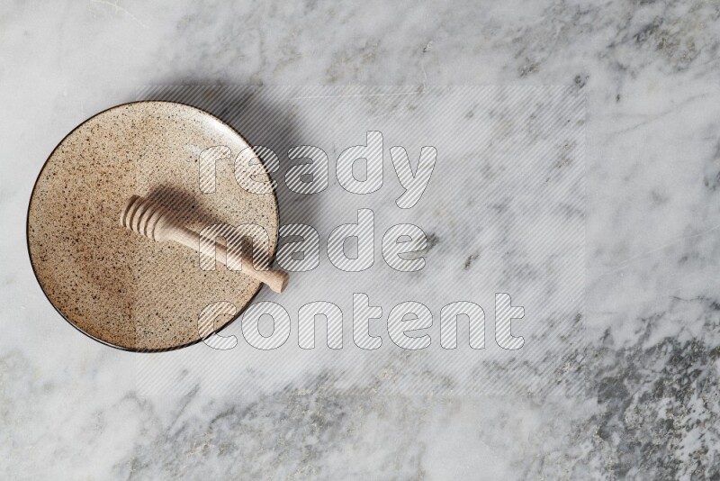 Multicolored pottery plate with wooden honey dipper in it on grey marble background