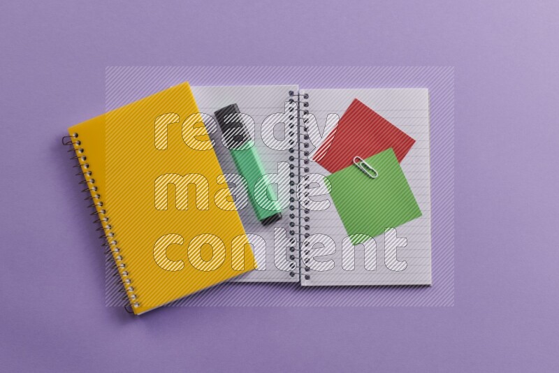 A yellow notebook with school supplies on purple background
