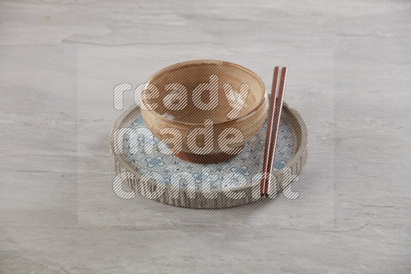 multi color pottery round bowl on top of multi color round ceramic plate and chopsticks, on grey textured countertop