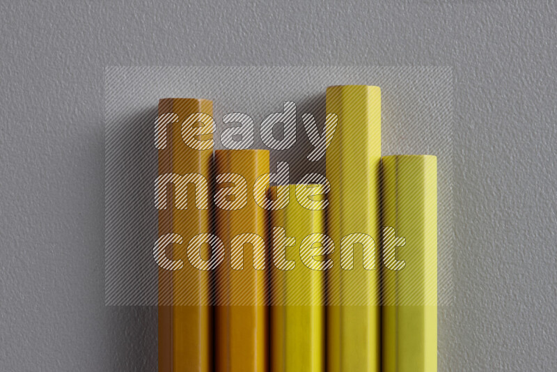 A collection of sharpened colored pencils arranged showcasing a gradient of yellow and orange hues on grey background