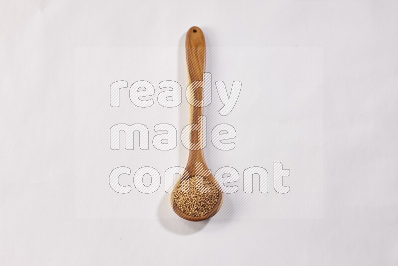 A wooden ladle full of mustard seeds on a white flooring