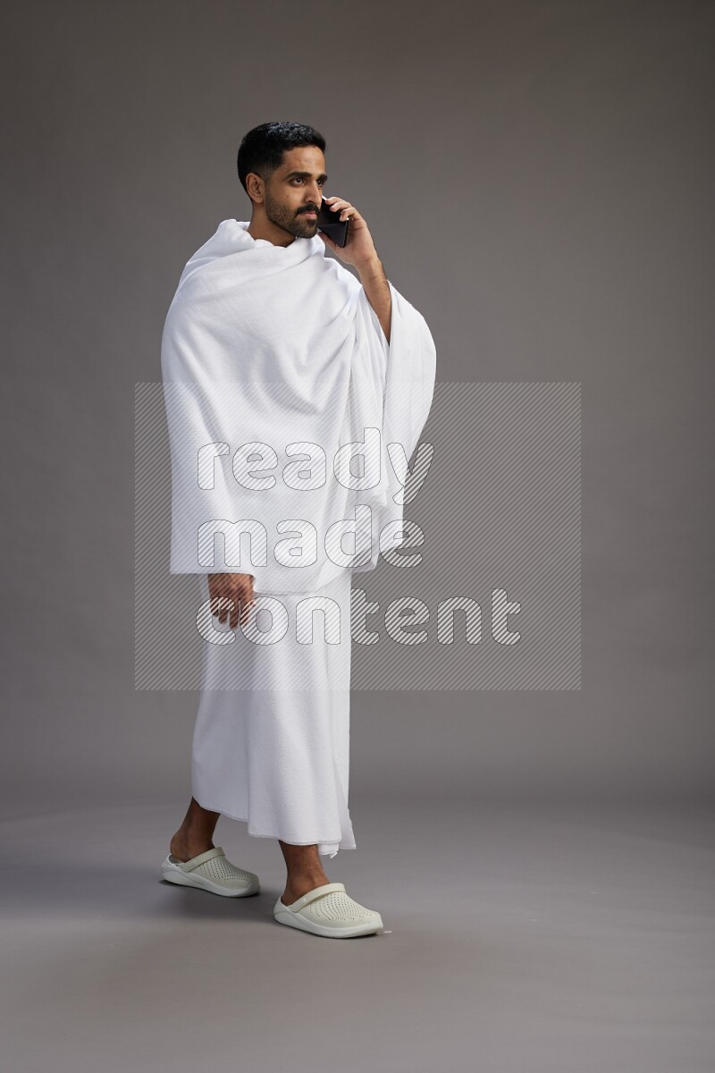 A man wearing Ehram Standing talking on phone on gray background