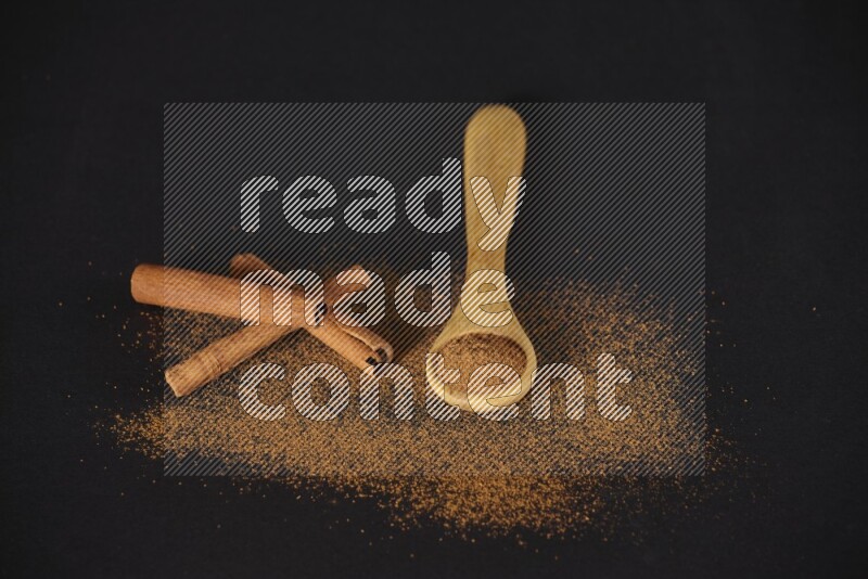 Cinnamon powder in a wooden spoon and cinnamon sticks beside it on black background