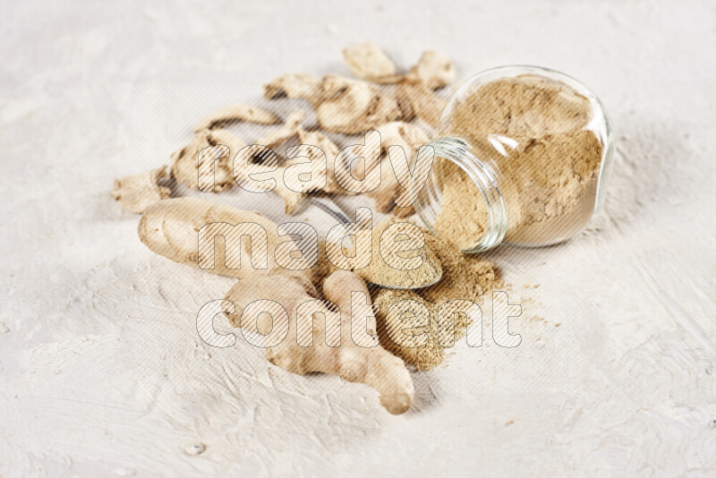 A glass jar full of ground ginger powder flipped with some spilling powder on white background