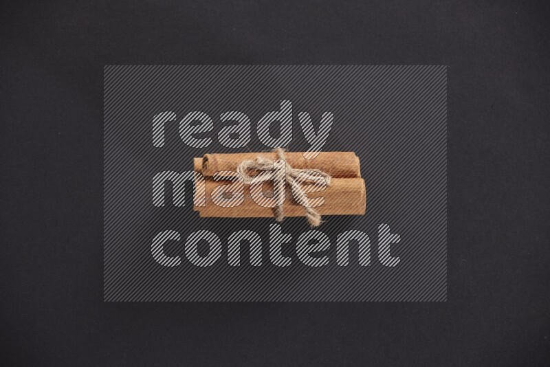 4 Cinnamon sticks stacked and bounded on black flooring