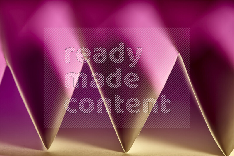 A close-up abstract image showing sharp geometric paper folds in pink gradients and warm tones
