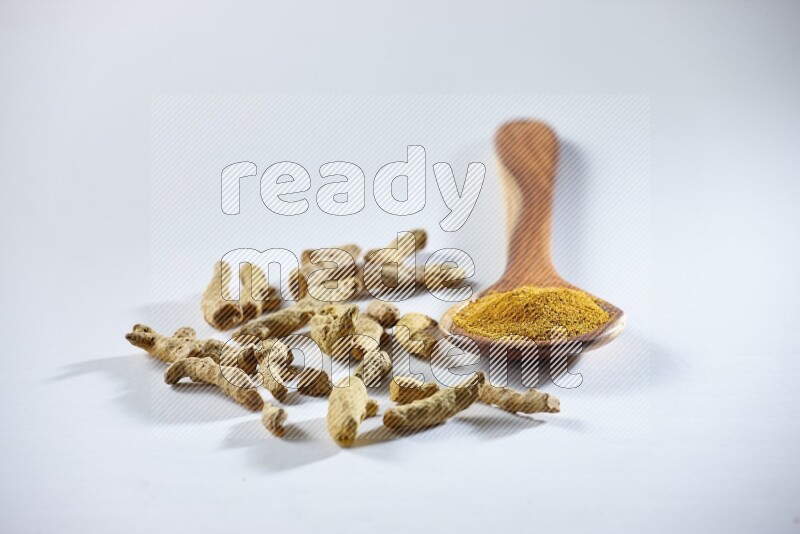 A wooden ladle full of turmeric powder and dried turmeric fingers beside it on white flooring