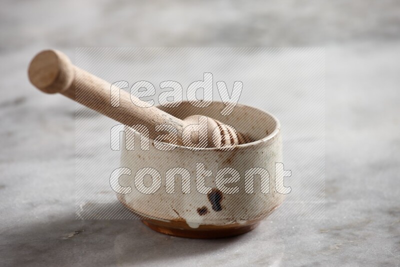 Multicolored pottery bowl with wooden honey dipper in it on grey marble background