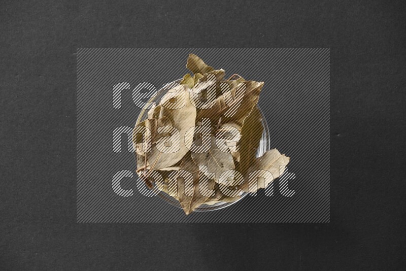 A glass bowl full of laurel leaves on black flooring