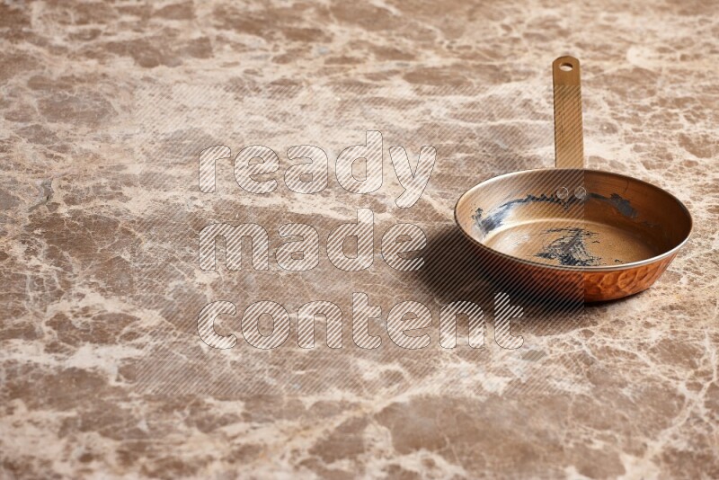 A small copper pan on beige marble background