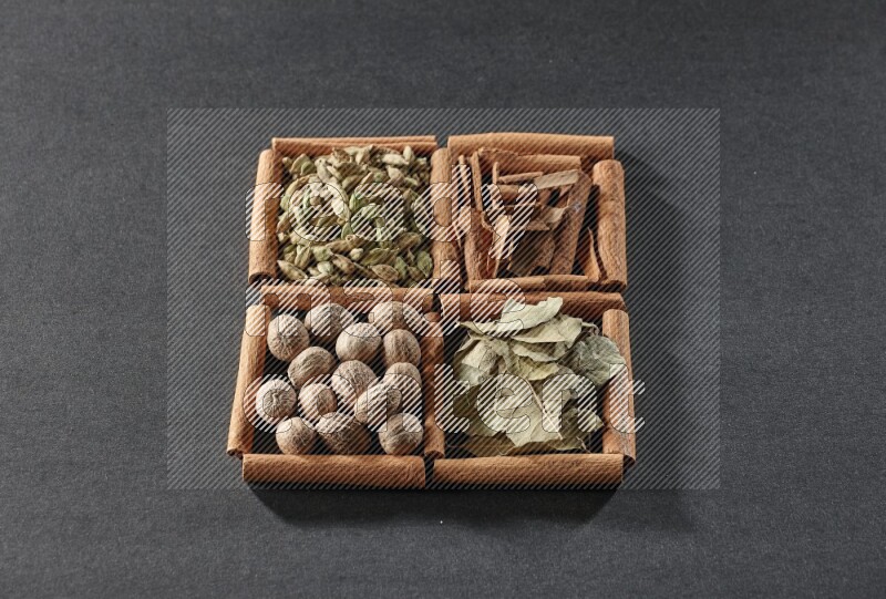 4 squares of cinnamon sticks full of cinnamon, cardamom, bay laurel leaves and nutmegs on black flooring