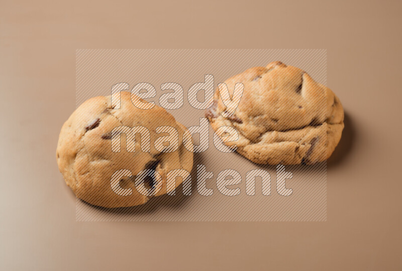 Two chocolate chip cookies on a brown background