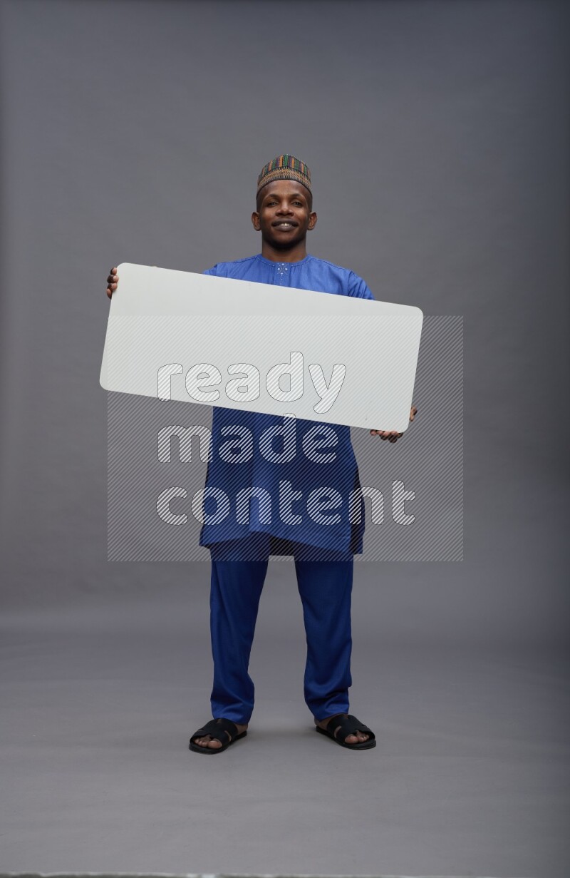 Man wearing Nigerian outfit standing holding board on gray background