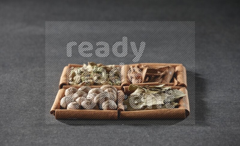4 squares of cinnamon sticks full of cinnamon, cardamom, bay laurel leaves and nutmegs on black flooring