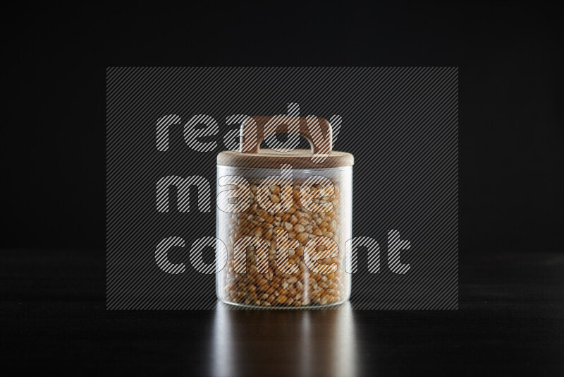Dry corn kernels in a glass jar on black background