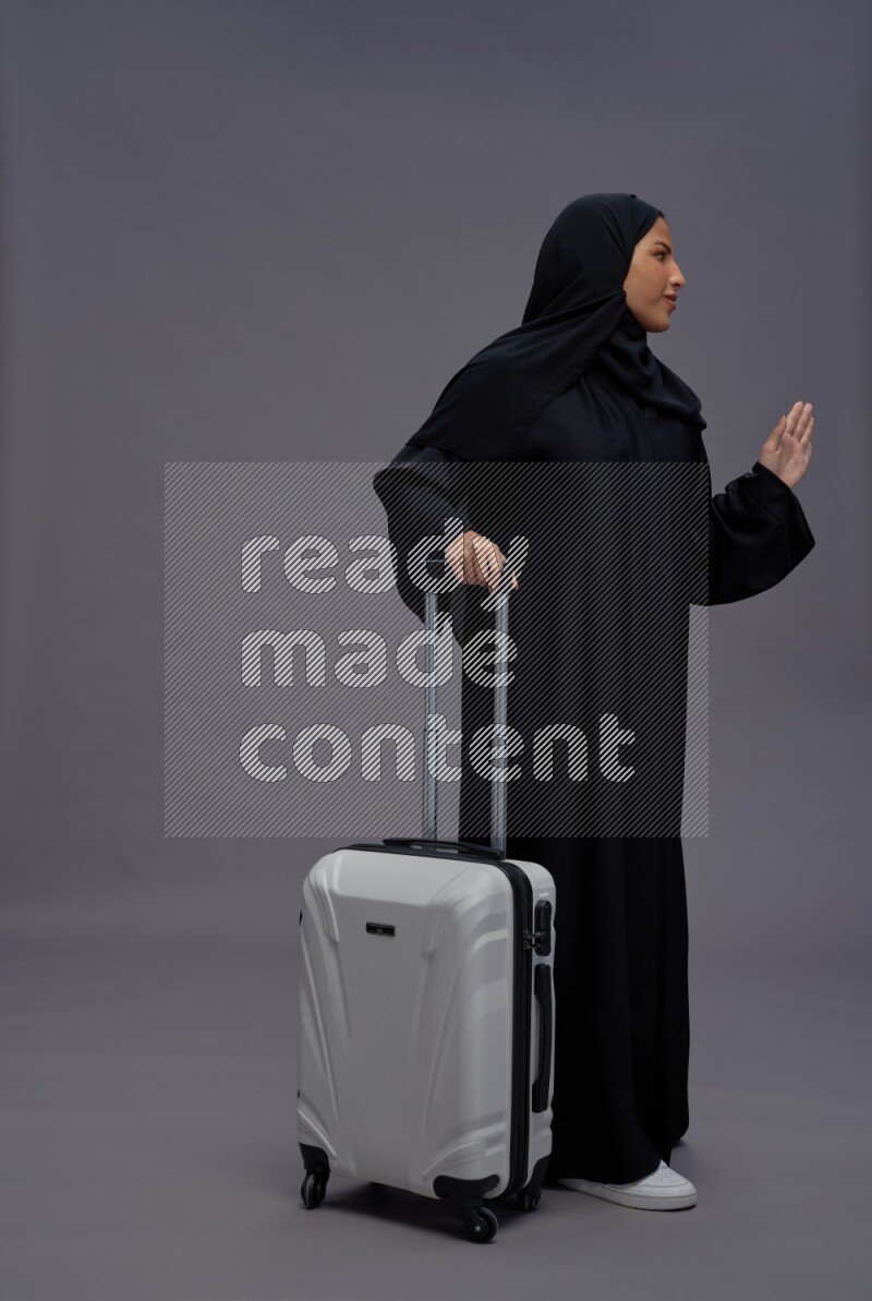 Saudi woman wearing Abaya standing holding bag on gray background