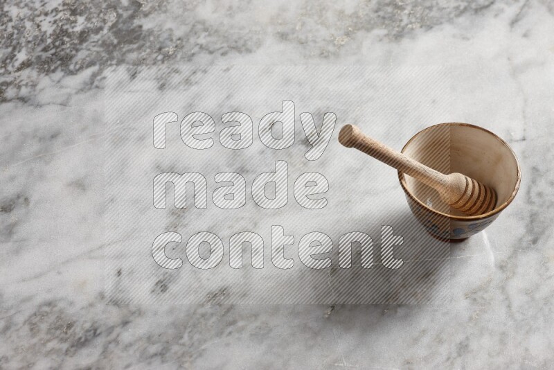 Decorative pottery bowl with wooden honey dipper in it on grey marble background