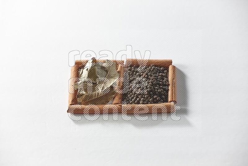 مربعان من أعواد القرفة ممتلئان بحبوب الفلفل الأسود وأوراق الغار علي خلفية بيضاء