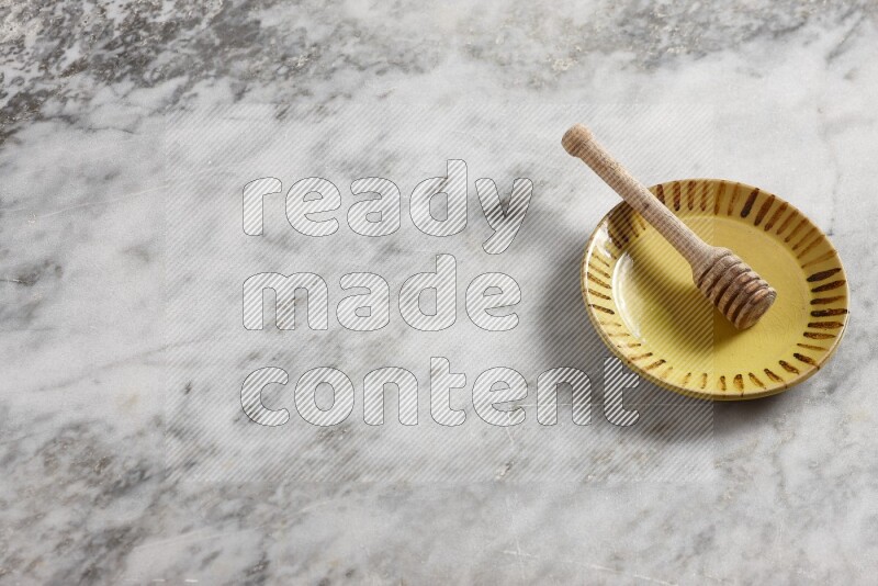 Multicolored pottery plate with wooden honey dipper in it on grey marble background