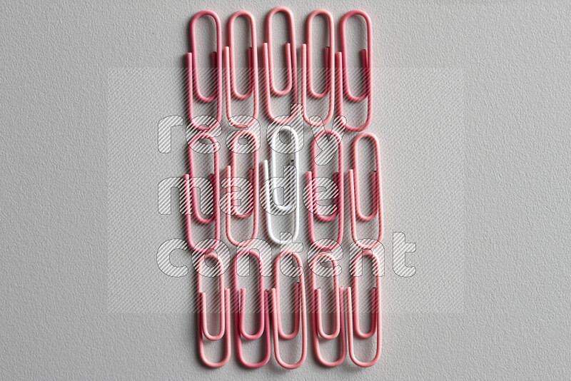 A bunch of pink paper clips with a different colored paper clip in the center on grey background