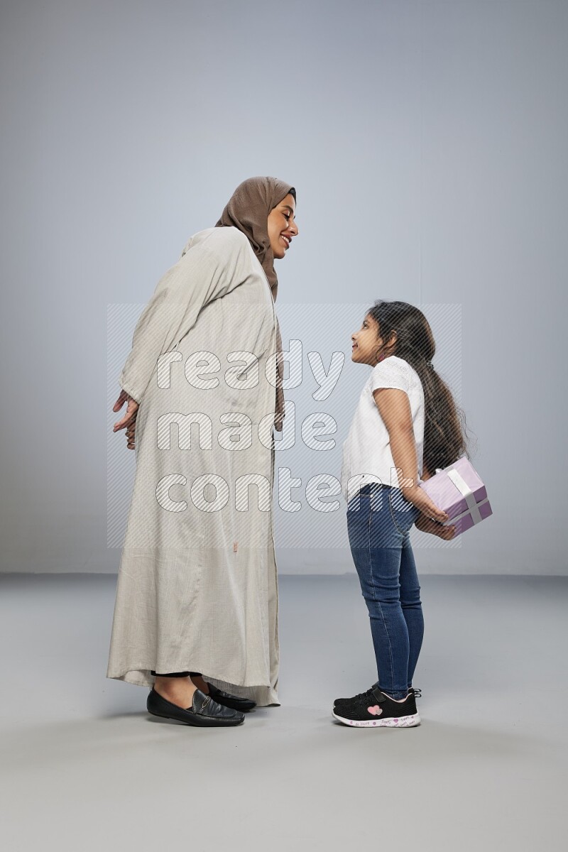 A girl standing hiding a gift behind her back for her mother on gray background