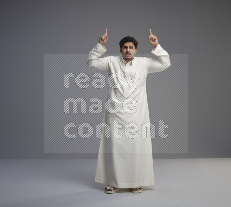 A Saudi man standing wearing thob interacting with the camera on gray background