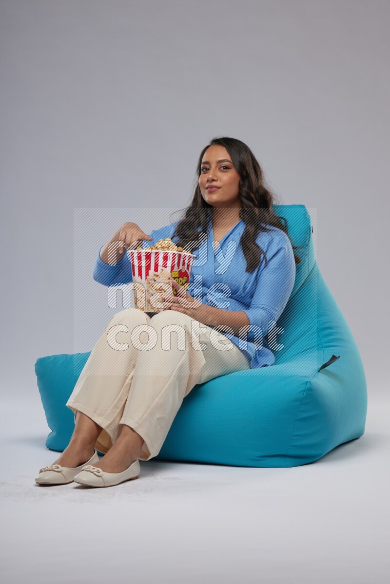 A woman sitting on a blue beanbag and eating popcorn