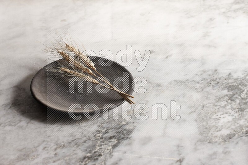 Wheat stalks on black pottery plate on grey marble background
