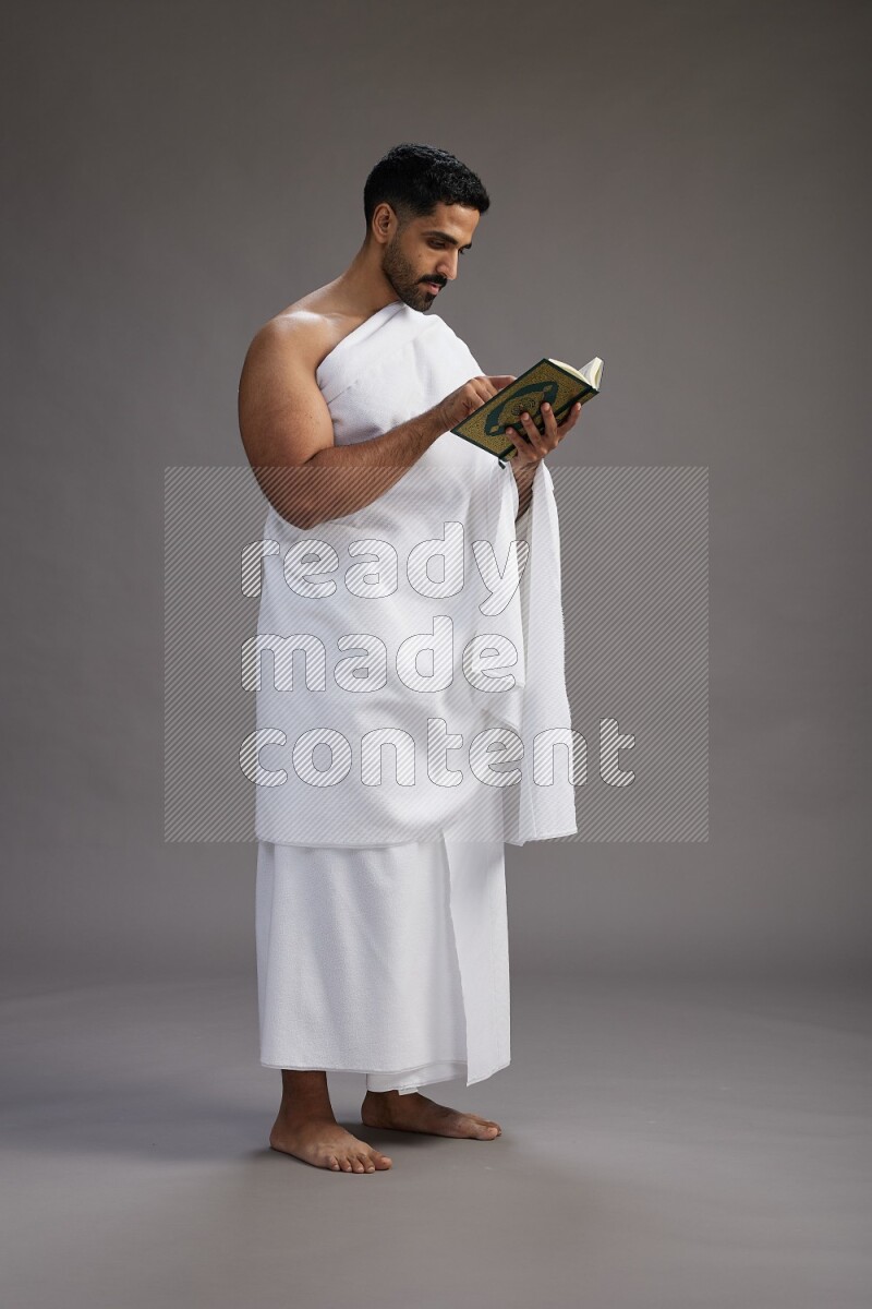 A man wearing Ehram Standing reading quran on gray background