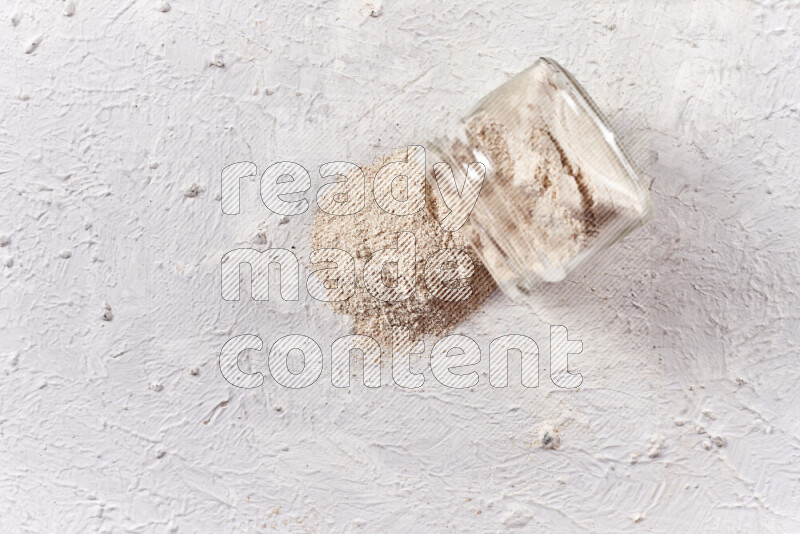 A glass jar full of onion powder flipped with some spilling powder on white background