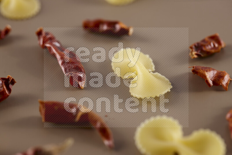 Raw pasta with different ingredients such as cherry tomatoes, garlic, onions, red chilis, black pepper, white pepper, bay laurel leaves, rosemary and cardamom on beige background
