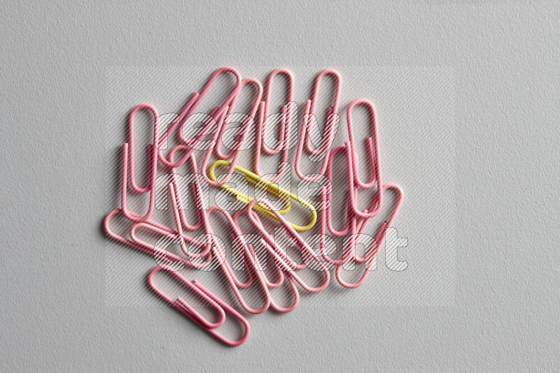A bunch of pink paper clips with a different colored paper clip in the center on grey background