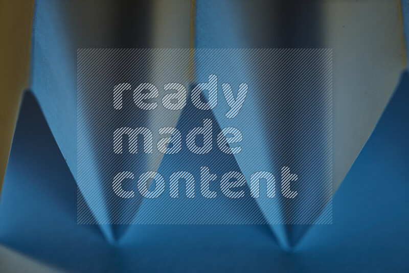 A close-up abstract image showing sharp geometric paper folds in blue gradients and warm tones